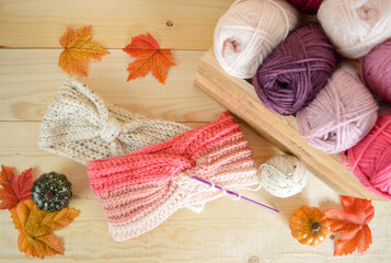 handmade crochet headband with woolen balls and crochet hooks, fall leaves on wooden ground