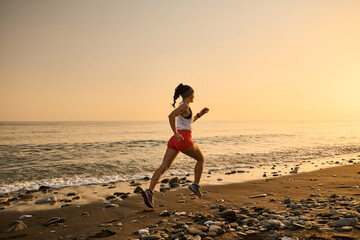 young woman enjoying a run in a pebbly beach at the sunset