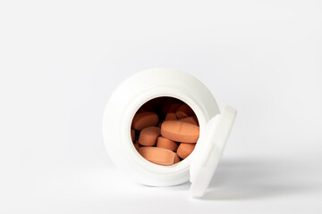 Orange pills in a white pill bottle on white background