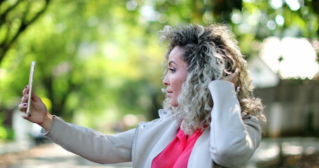 Woman adjusting hair and face in front of cellphone camera outside