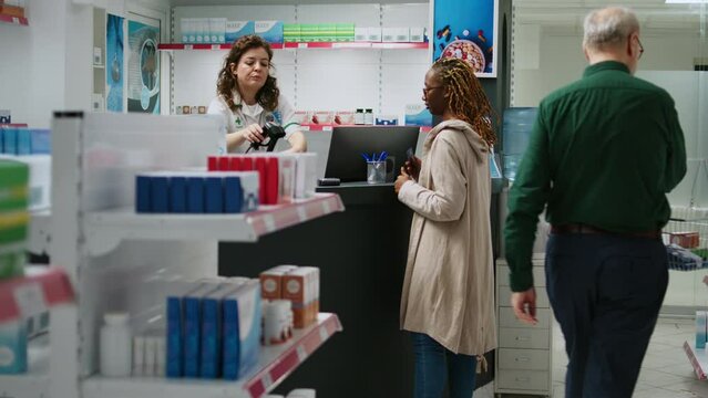 African american client buying pharmaceutical products and paying with credit card at pharmacy counter. Using contactless payment to buy medicaments and healthcare supplements at drugstore.