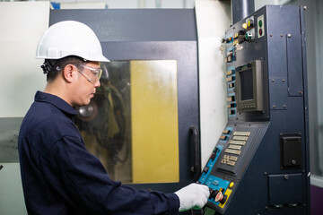 Asian male engineer foreman or mechanic worker controlling industry metal machine at industrial factory. man working at construction site in safety helmet and blue collar