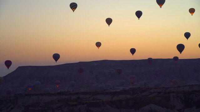 Balloons against backdrop of mountains and pink sky without clouds ea dawn. Balloons in sky in Cappadocia in Turkey. many small balloons flying in sky at dawn.