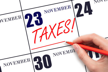 Hand drawing red line and writing the text Taxes on calendar date November 23. Remind date of tax payment