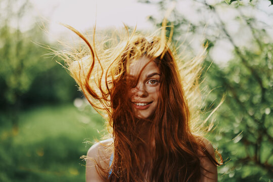 Woman portrait smile happiness catch looks into the camera with a smile with teeth spring flying hair long red, the concept of health and beauty hair sunset