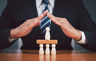A businessman's hands protect a wooden peg doll that is like a top executive protecting the members...