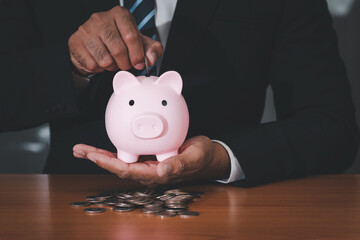 A businessman holds a piggy bank while putting coins into the piggy bank to save money. money saving and financial concept.