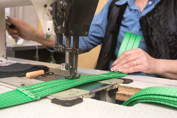 Industrial sewing machine sews a webbing sling. Manufacture of textile slings and tie straps.
