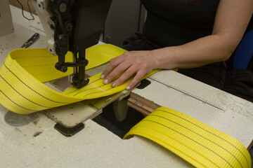 Industrial sewing machine sews a webbing sling. Manufacture of textile slings and tie straps.