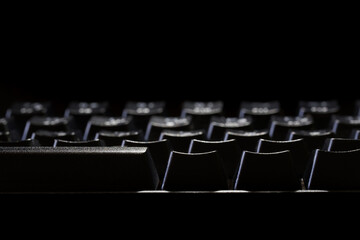 Fototapeta premium Black gaming mechanical computer keyboard on a black background. Fragment. Copy space. Macro. Selective focus. Depth of the dark space. Preparation for advertising.