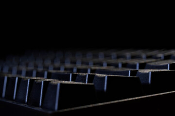 Black mechanical gaming computer keyboard on a black background. Side view. Copy space. Macro. Selective focus. Depth of space and bokeh.