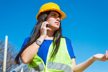 young woman worker with safety helmet outdoors angry and indignant on a phone call