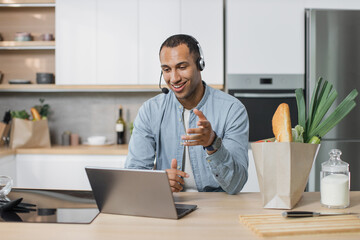 Young arab man, chef sitting in well-equipped modern kitchen having online video conversation with subscribers during vlog session how to cook delicious salad for breakfast looking at laptop .