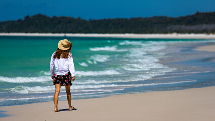 beautiful girl in dress and shirt and hat walks on paradise beach with white sand and turquoise water; walk on whitehaven beach on whitsunday island in queensland; paradise beaches of australia; sunny