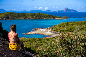 A beautiful girl sits on top of a mountain overlooking a panorama of the whitsunday islands;...