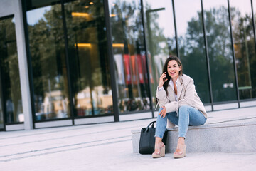 Young cheerful business woman working with a mobile phone in the street with office buildings in the background