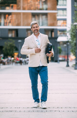 Cheerful middle age businessman walking by street towards modern office building, going to job in the morning