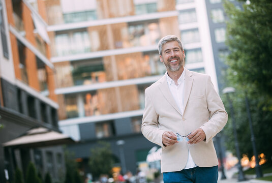 Cheerful Middle Age Businessman In Glasses Walking By Street Towards Modern Office Building, Going To Job In The Morning