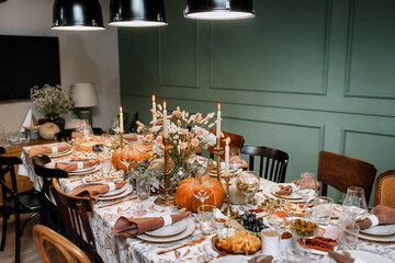 Decoration and serving of the festive table with autumn decor, candles and flowers and pumpkins and dishes.