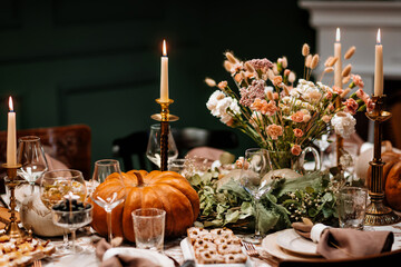 Decoration and serving of the festive table with autumn decor, candles and flowers and pumpkins and dishes.