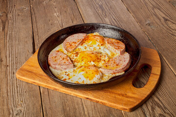 Fried eggs with sausage in a frying pan on a wooden table.