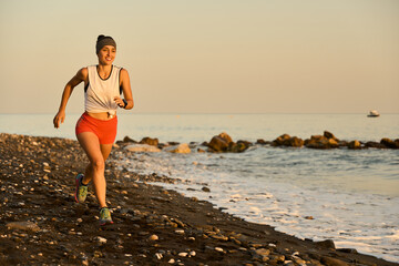 young woman enjoying a run in a pebbly beach at the sunset