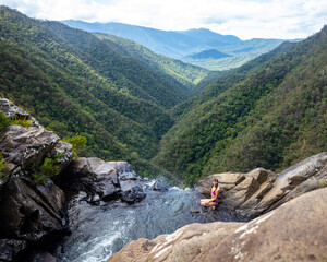 beautiful girl in bikini sits over precipice at top of windin falls; scary waterfall in atherton tablelands, queensland, australia, pool at top of waterfall