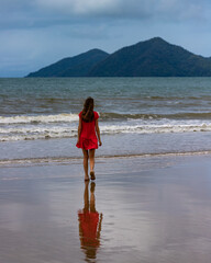 long-haired girl in red dress walks along tropical Australian beach with islands in the background; vacation in queensland, australia, northern tropical queensland