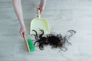 Caucasian woman sweeping the floor with a brush and dustpan in hairdressing salon. Cropped hair on...