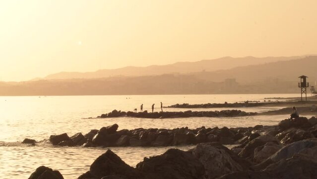 Sunset in the beach shore with kids playing in the rocks