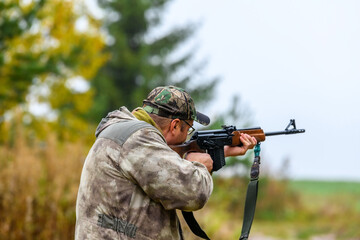 A man takes aim and shoots a combat carbine or guns in blurry focus at targets in a shooting range. Back view of a shooting hunter during hunting.
