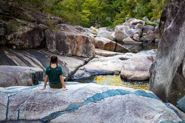 girl with pigtails sits on colorful rocks at jourama falls at sunset; relaxing at paluma range national park in queensland, australia; cascading waterfalls with pools