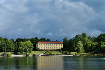 Fototapeta na wymiar Swedish castle is located in a beautiful park facing the waterfront. Dark clouds hang over an old mansion.