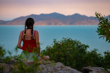 beautiful girl sitting top of mountain overlooking magnetic island skyline at sunset; relaxing on magnetic island, queensland, australia
