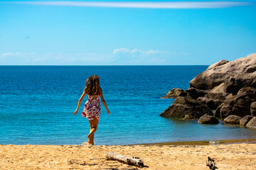 Fototapeta na wymiar a beautiful long-haired girl in a dress relaxes on a paradise beach on magnetic island; a beach with massive rocks and turquoise water; relaxing on magnetic island, queensland, australia