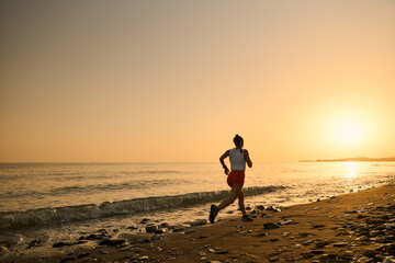 young woman enjoying a run in a pebbly beach at the sunset