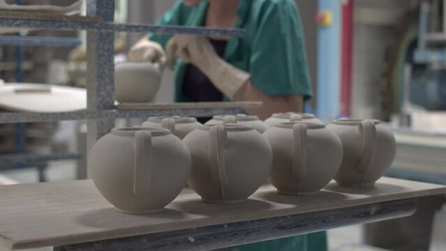 The porcelain factory workers are protected by newly made teapot molds with a knife. There is working equipment in the back.