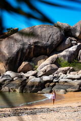 a beautiful long-haired girl in a dress relaxes on a paradise beach on magnetic island; a beach with massive rocks and turquoise water; relaxing on magnetic island, queensland, australia