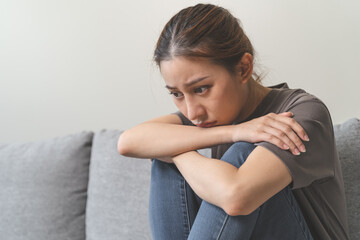 Unhappy anxiety young Asian woman covering her face with pillow on the cough in the living room at home. - obrazy, fototapety, plakaty