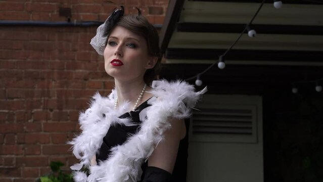 A brunette in a hat hugs herself with a white boa close-up. Slow motion of a young woman in a historical dress of the 20-30s of the XX century. High quality FullHD footage
