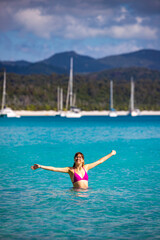 A beautiful girl in a bikini enjoys a dip in the turquoise water on whitehaven beach; relaxing on paradise beaches on whitsunday islands, queensland, australia