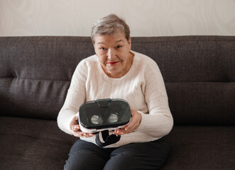 An elderly woman is looking at virtual reality glasses. Modern technologies. New experience in old person's life. Adaptation of pensioners in modern world. The idea of original gift for Mother's Day
