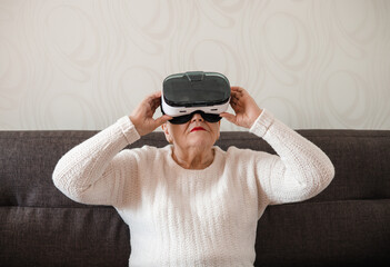 An elderly woman is playing using virtual reality glasses. Modern technologies. A new experience in...