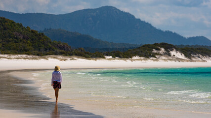 beautiful girl in dress and shirt and hat walks on paradise beach with white sand and turquoise water; walk on whitehaven beach on whitsunday island in queensland; paradise beaches of australia; sunny