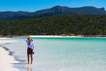 a beautiful girl in a dress, shirt and hat enjoys a walk on the white dunes at whitehaven beach; paradise beach with white sand and turquoise waters; whistundays island holiday, queensland, australia;