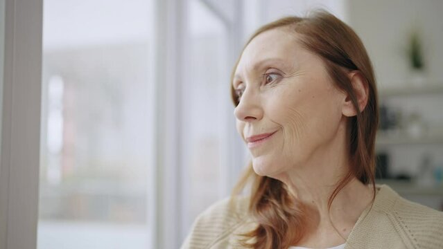 Attractive woman in her 60s looking out the window, in love, daydreaming