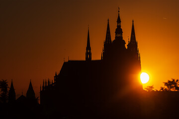 Fototapeta premium Sunrise behind Prague Castle which is silhouetted against the light orange sky.