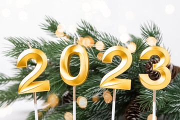 Christmas card with numbers 2023 in gold color and defocus lights, green fir branches in the background.