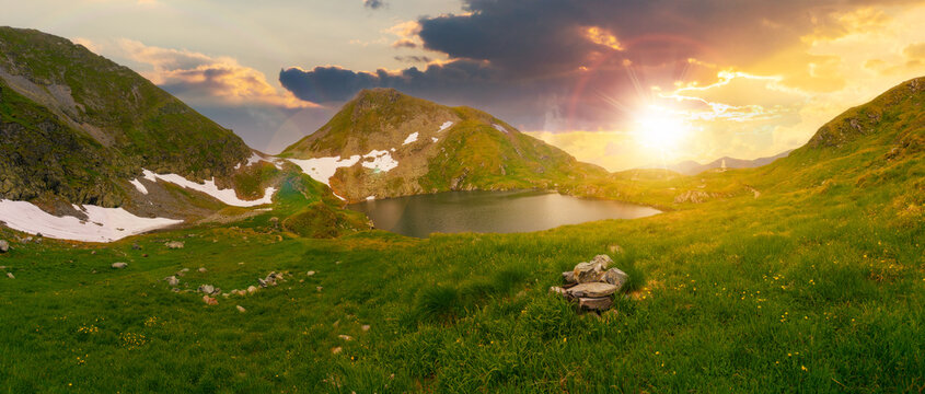 high altitude mountain lake at sunset. beautiful nature landscape of romania. grass and snow on the hills in evening light. sunny weather with clouds on the sky in summer
