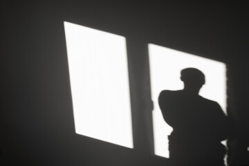 Silhouette of a man on reflected light from a window on a gray wall. Abstract background with shadow of a man.